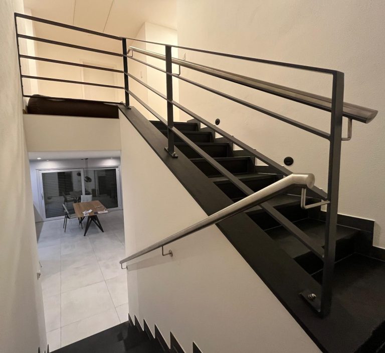 Geländer Pulverbeschichtet mit Edelstahlhandlauf Schlosserarbeit Schweißkonstruktion Architektur Handwerk Maßanfertigung Treppenhaus mit moderner Geländerkonstruktion und Blick auf den unteren Raum.